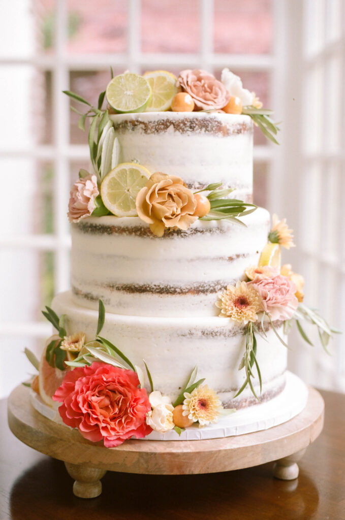 a naked wedding cake decorated with fresh flowers and citrus fruit